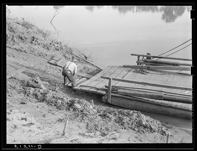 A man tying a ferry to the bank of a river