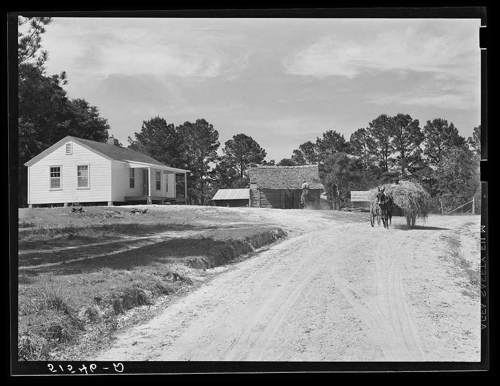 Dirt driveway leading up to a new and old home beside each other