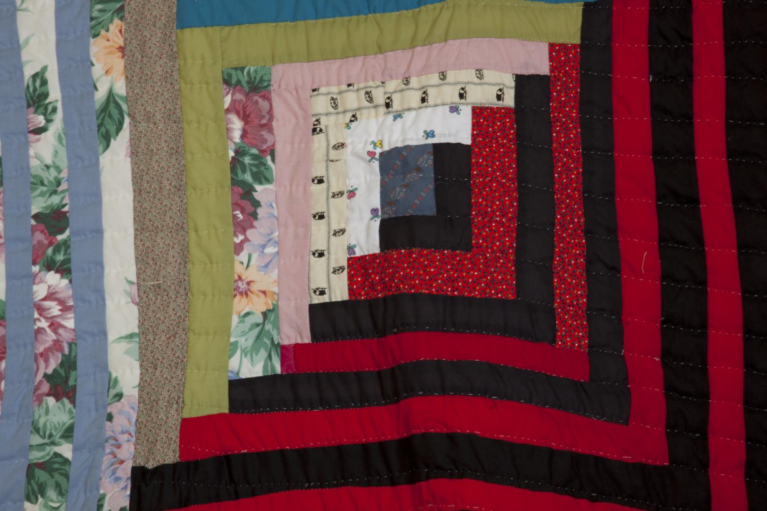 Quilt with fabric strips forming right angles; the top left half is of floral, pastel strips, the bottom right half is of mostly solid black and red strips